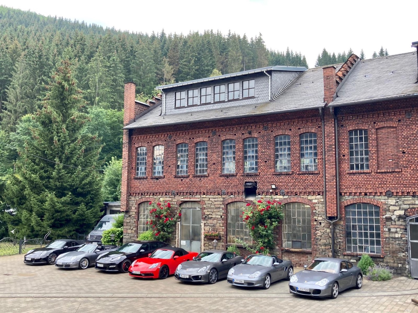 Group of Porsches at a historic industrial site surrounded by forest